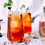 Iced Tea that is styled with a sprig of a green herb. There are roses in the background.
