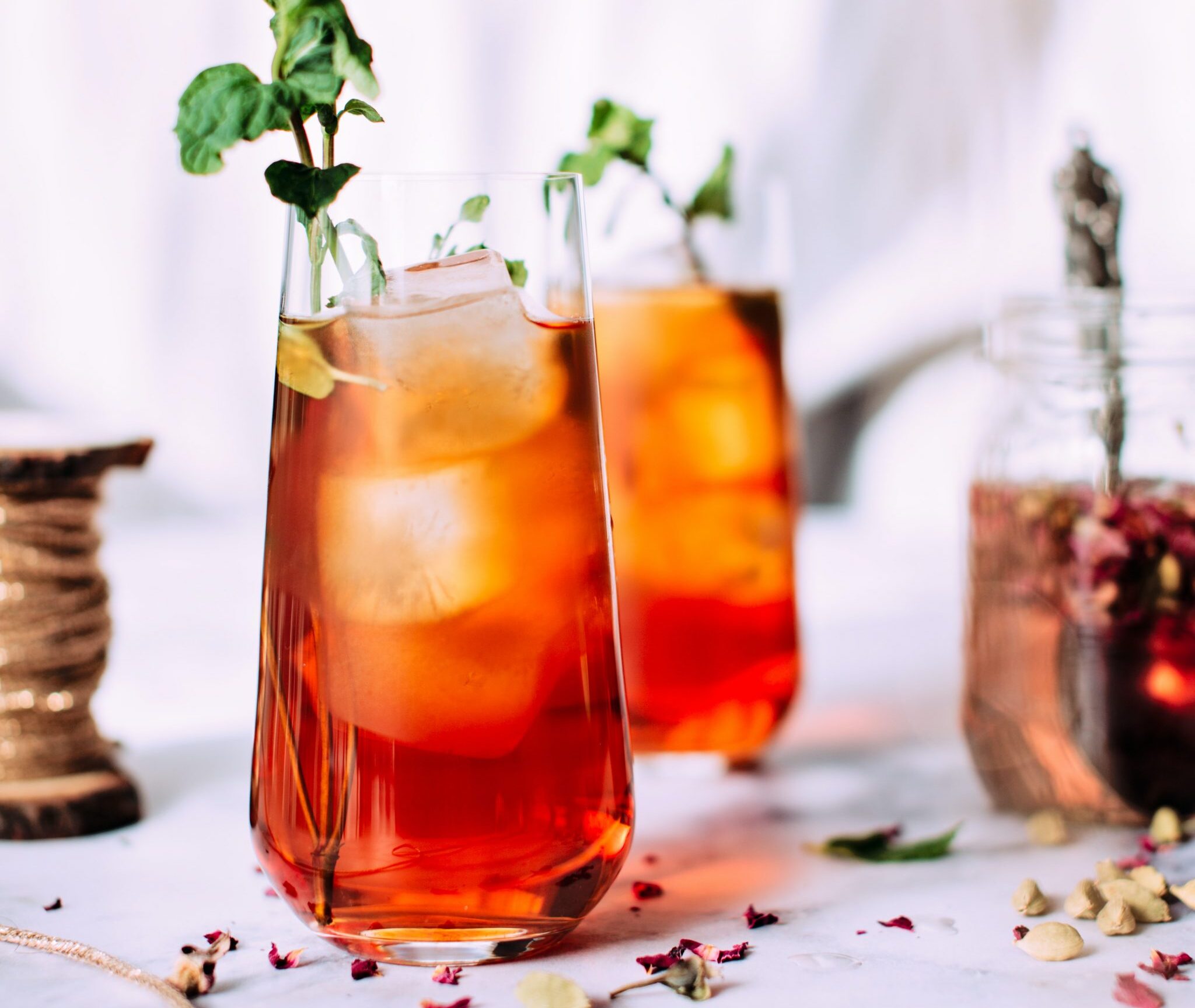 Iced Tea that is styled with a sprig of a green herb. There are roses in the background.