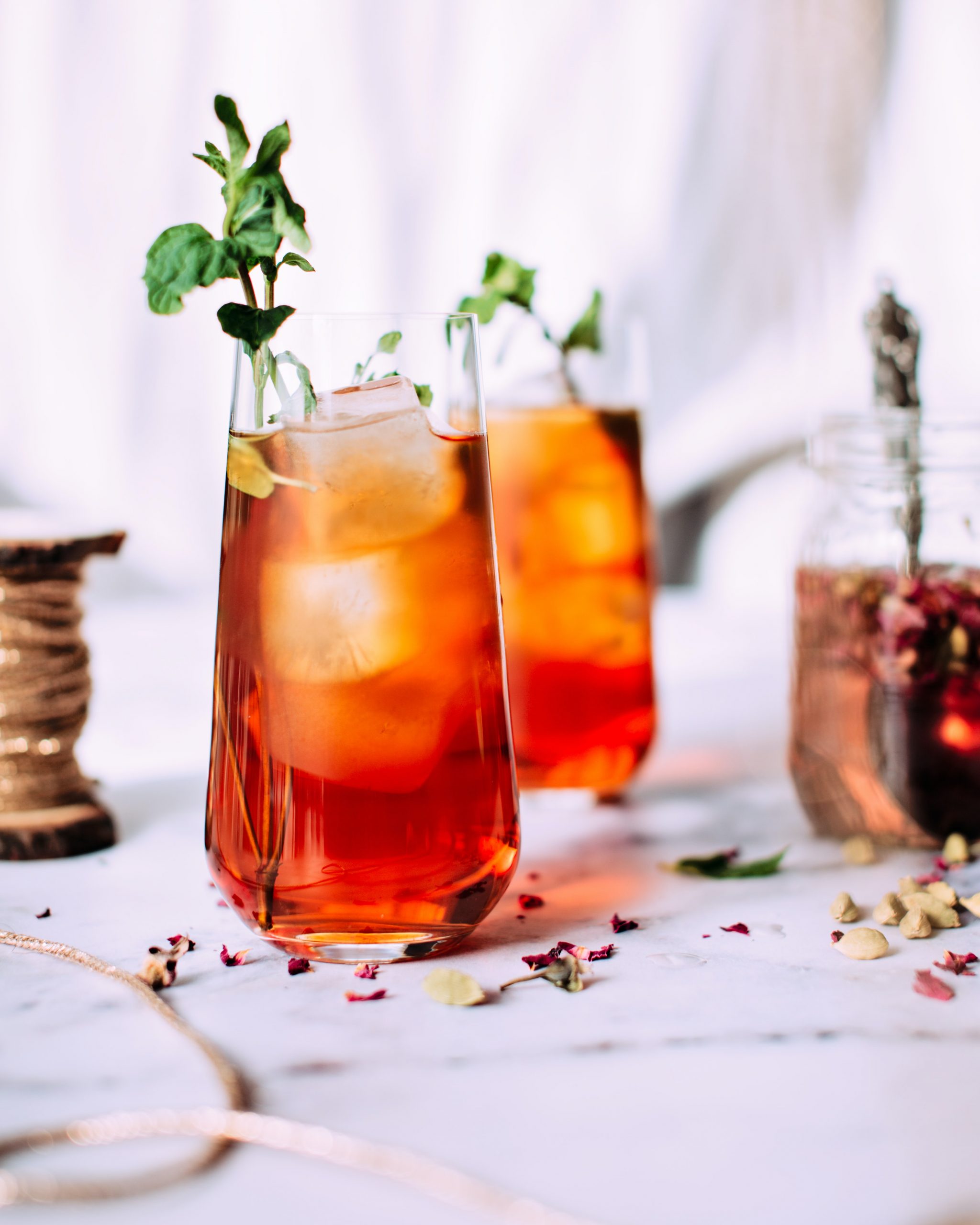Iced Tea that is styled with a sprig of a green herb. There are roses in the background.